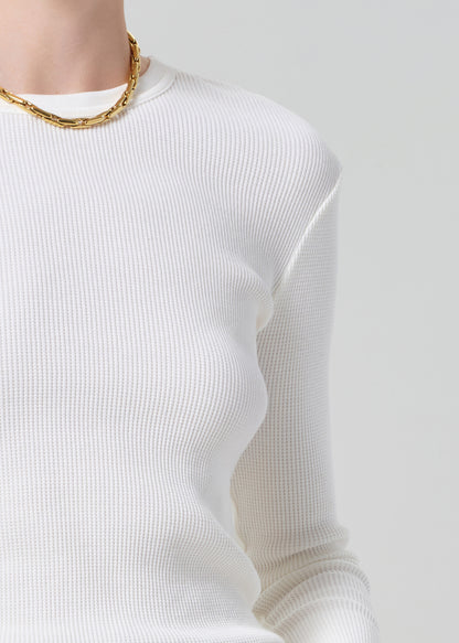 Person wearing a white long-sleeve top and blue jeans with a gold belt on a gray background