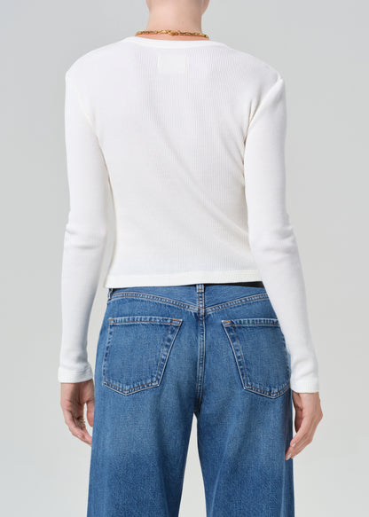 Person wearing a white long-sleeve top and blue jeans with a gold belt on a gray background