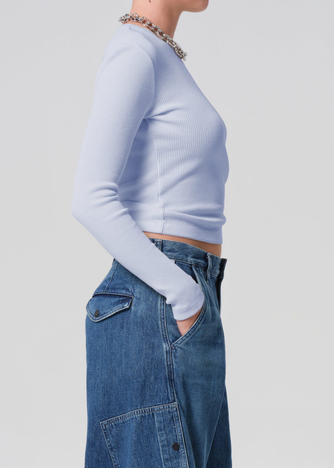 Person wearing a light blue long-sleeve top and blue jeans on a plain background