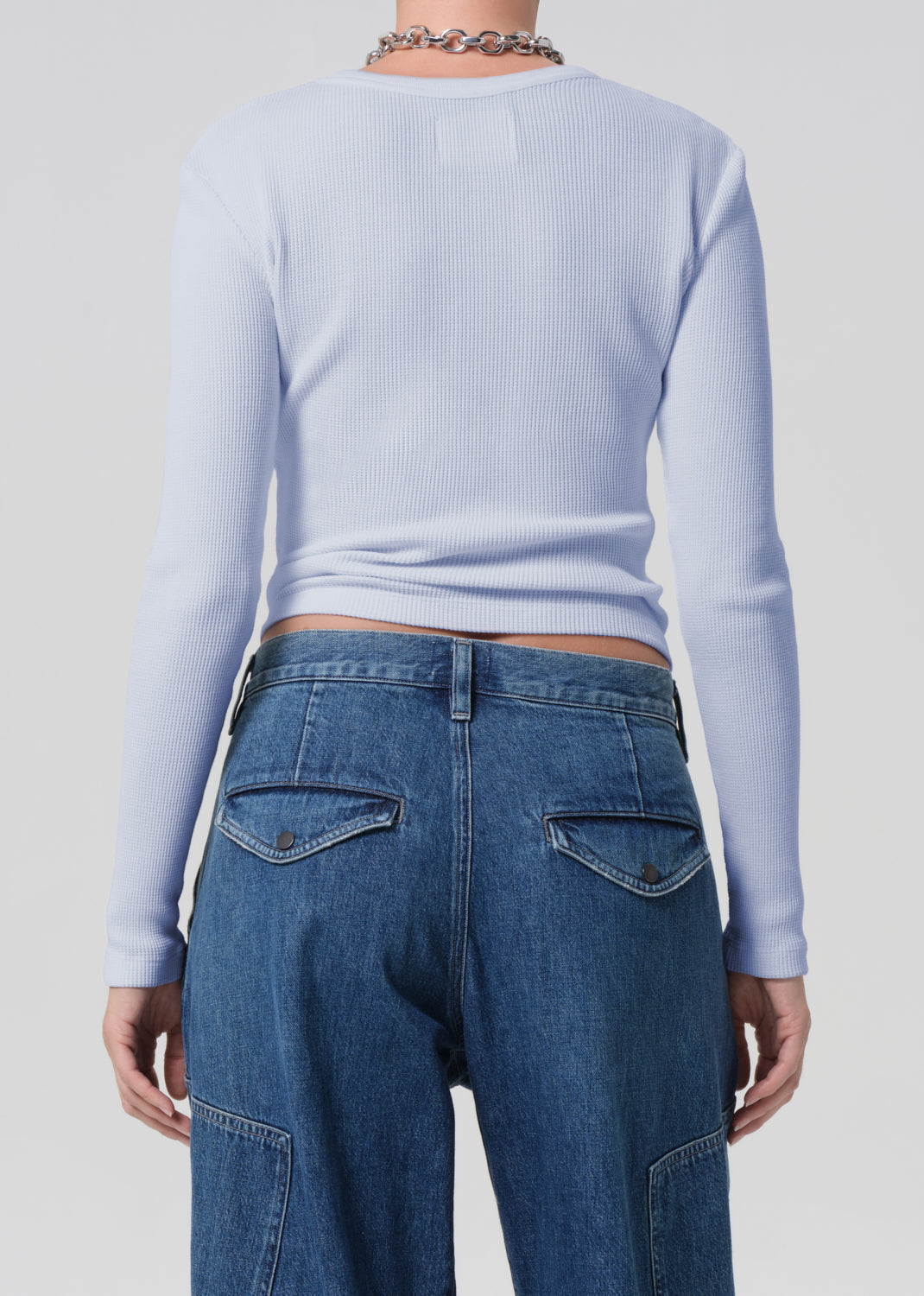 Person wearing a light blue long-sleeve top and blue jeans on a plain background