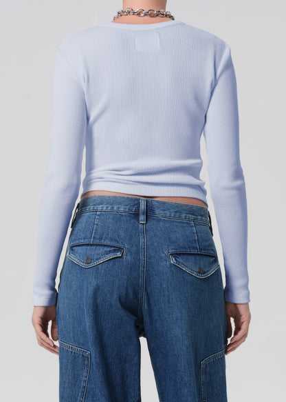 Person wearing a light blue long-sleeve top and blue jeans on a plain background