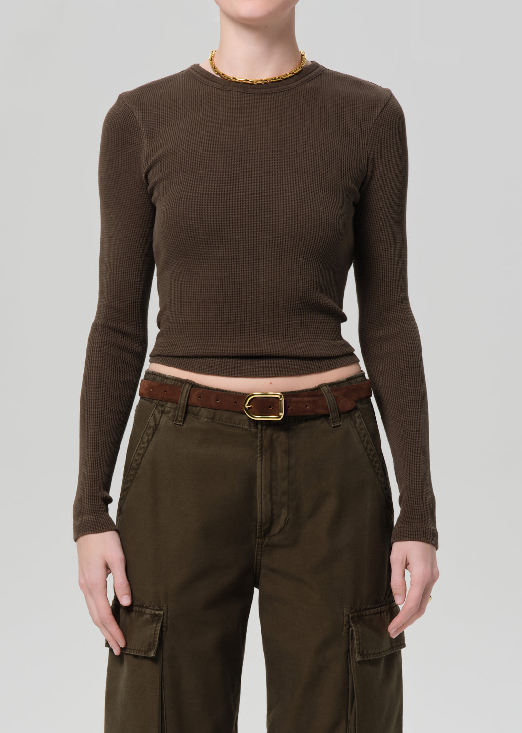 Person wearing a brown long-sleeve top and cargo pants on a plain background