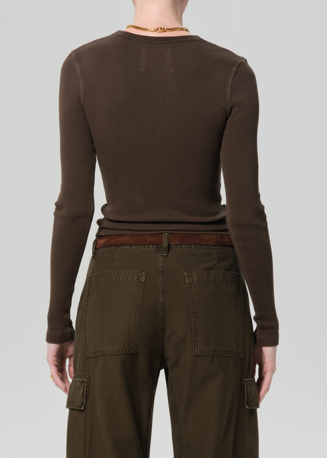 Person wearing a brown long-sleeve top and cargo pants on a plain background