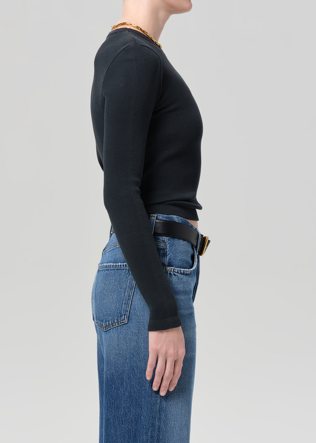 Person wearing a black long-sleeve top and blue jeans on a gray background