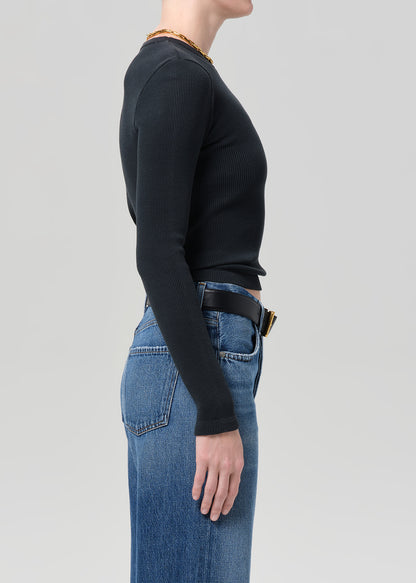 Person wearing a black long-sleeve top and blue jeans on a gray background