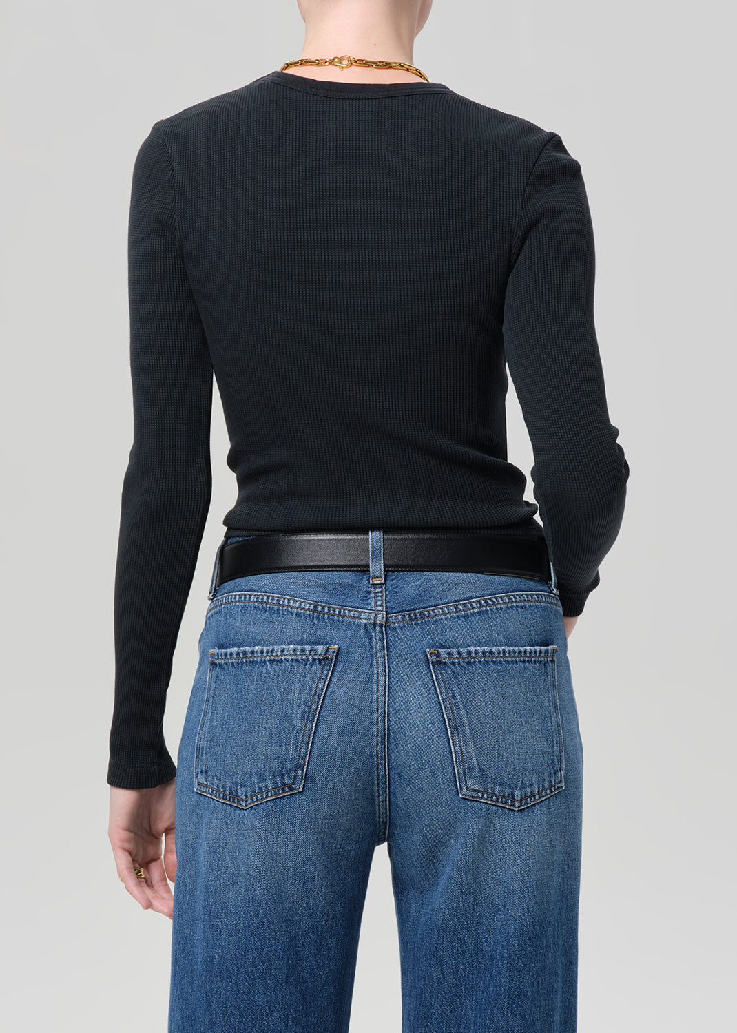 Person wearing a black long-sleeve top and blue jeans on a light gray background