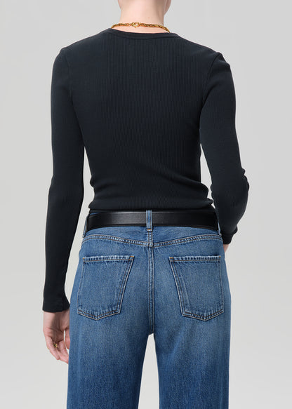 Person wearing a black long-sleeve top and blue jeans on a light gray background
