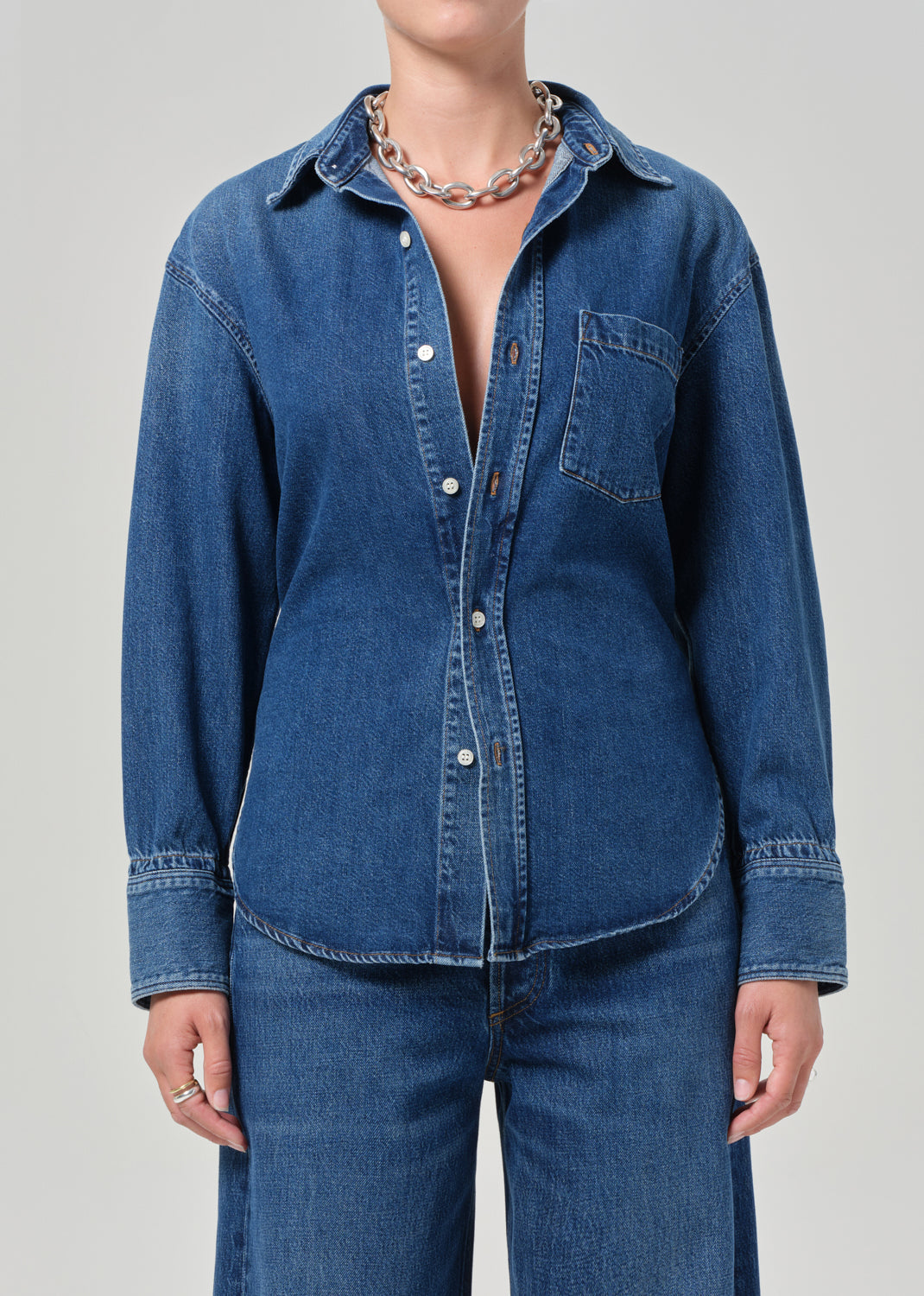 Person wearing a blue denim shirt and jeans on a gray background