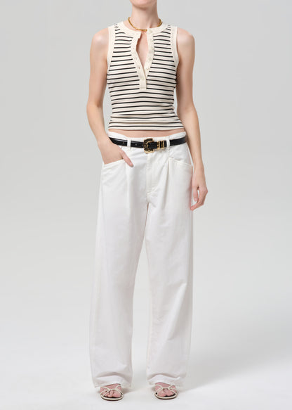 Person wearing a striped sleeveless top and white pants on a plain background