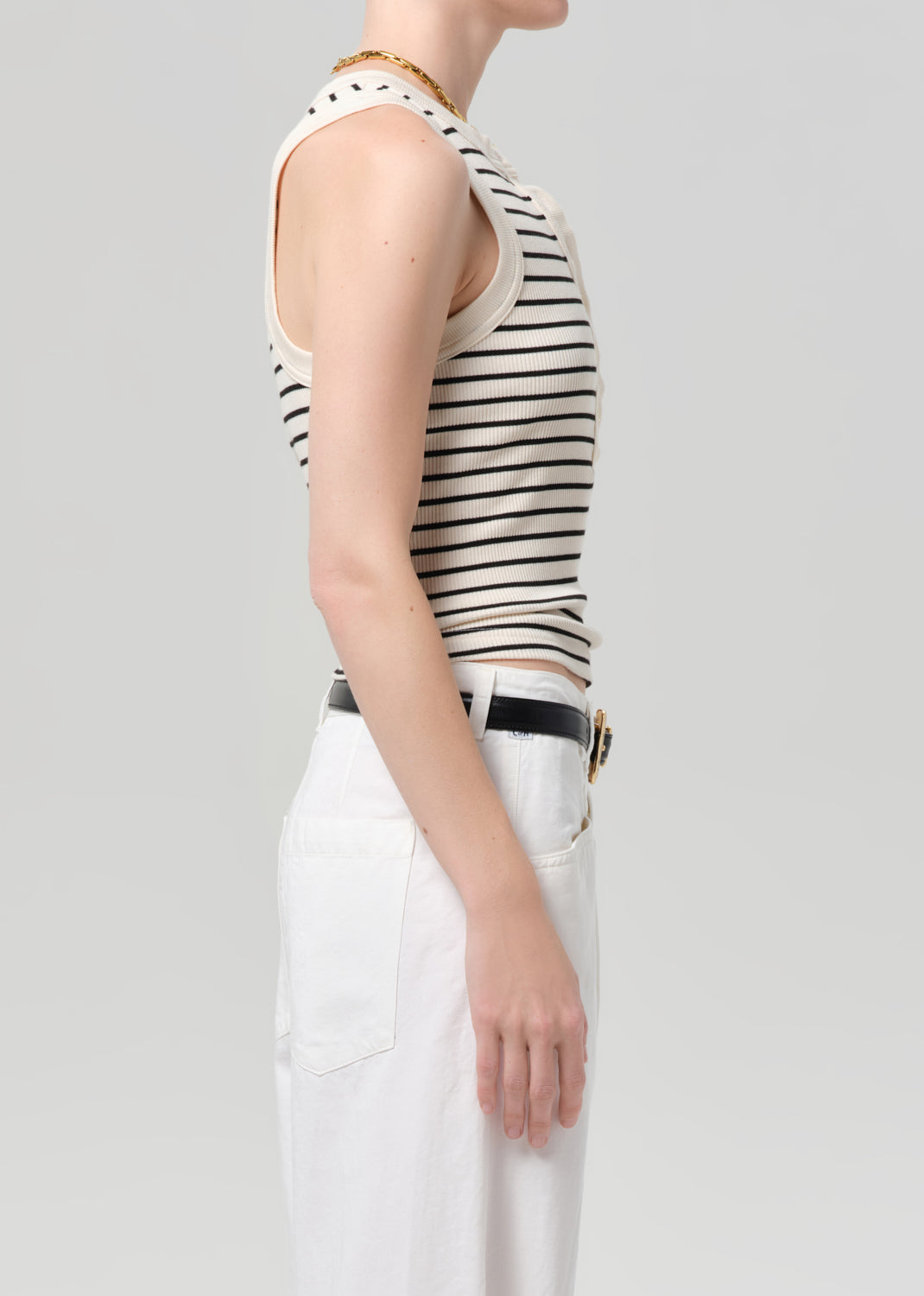 Person wearing a striped sleeveless top and white pants on a plain background