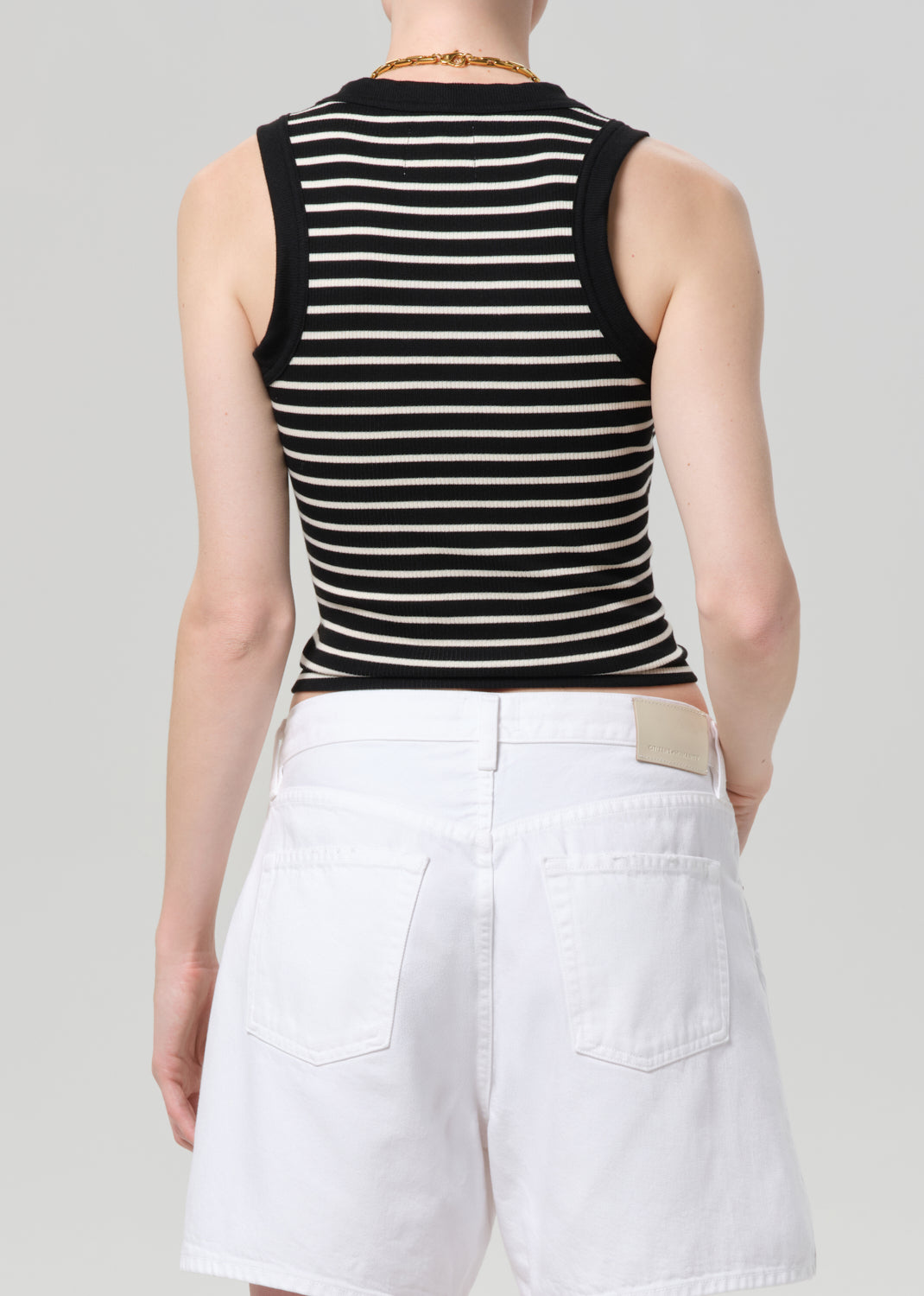 Person wearing a black and white striped sleeveless top with a deep neckline and white shorts on a gray background.