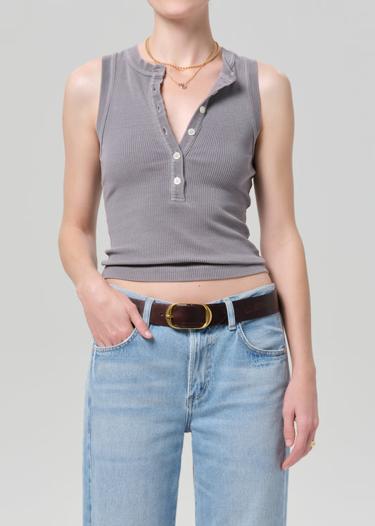 Person wearing a gray sleeveless henley top and blue jeans on a plain background