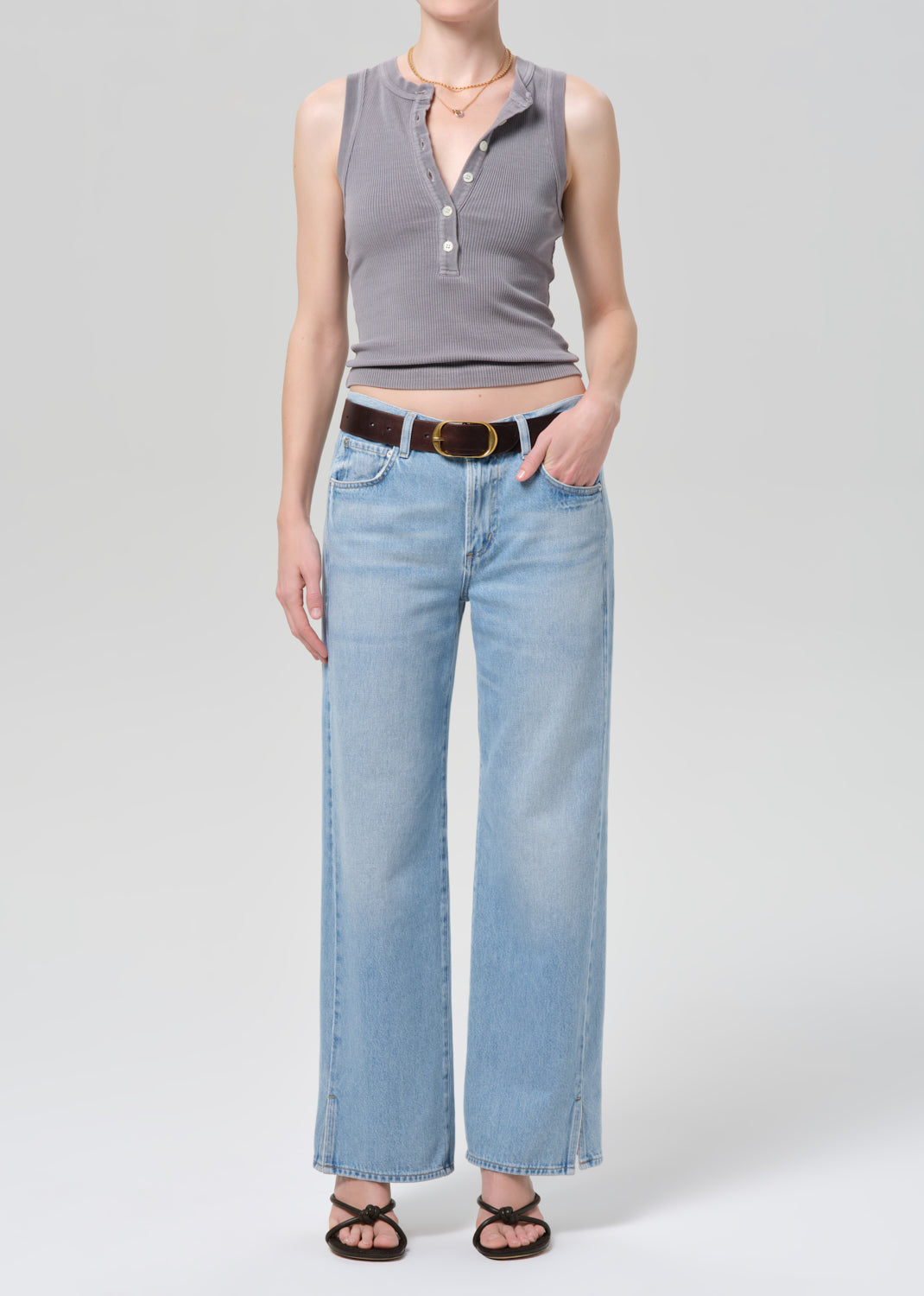 Person wearing a gray sleeveless top and light blue jeans on a plain background