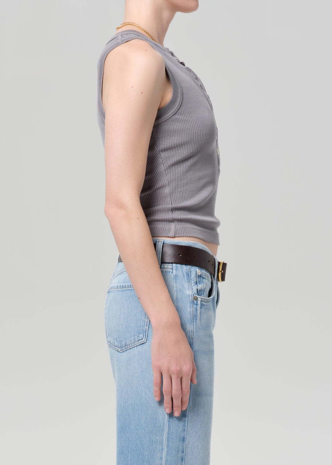 Person wearing a gray tank top and blue jeans on a light gray background