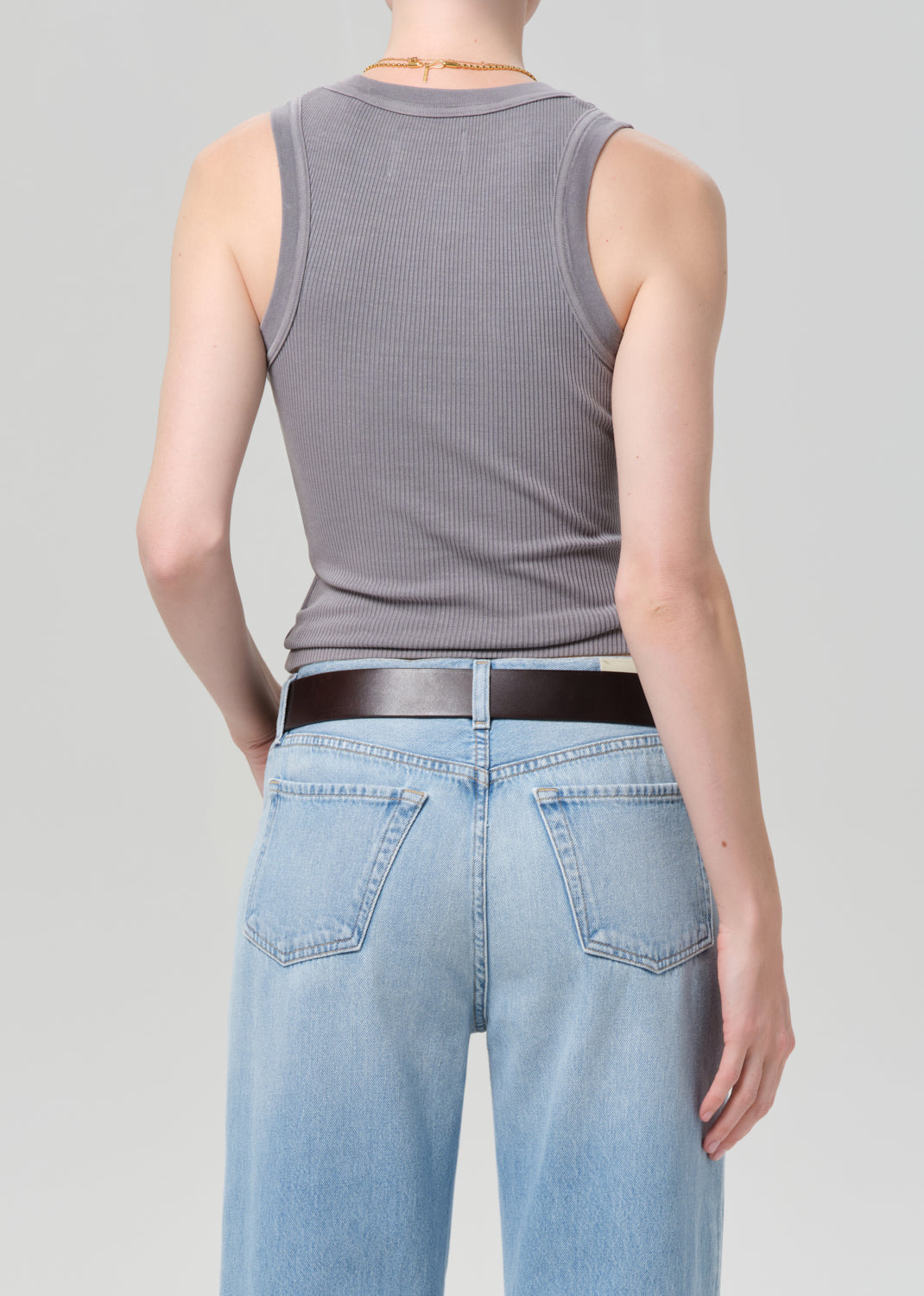 Person wearing a gray ribbed tank top and light blue jeans on a plain background