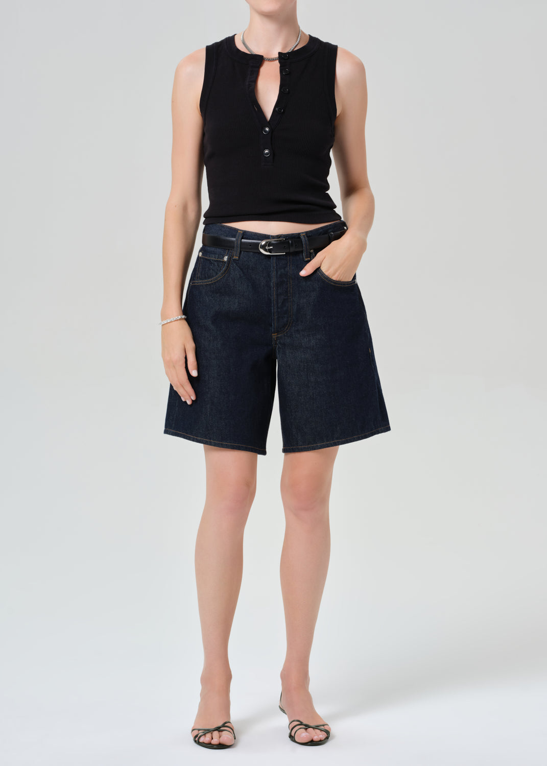 Person wearing a black sleeveless top and dark blue denim shorts on a gray background
