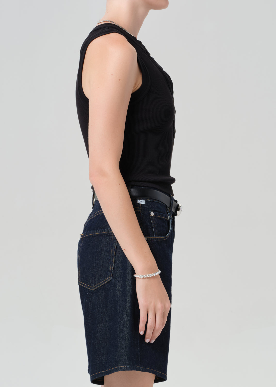 Person wearing a black sleeveless top and dark blue denim shorts on a gray background