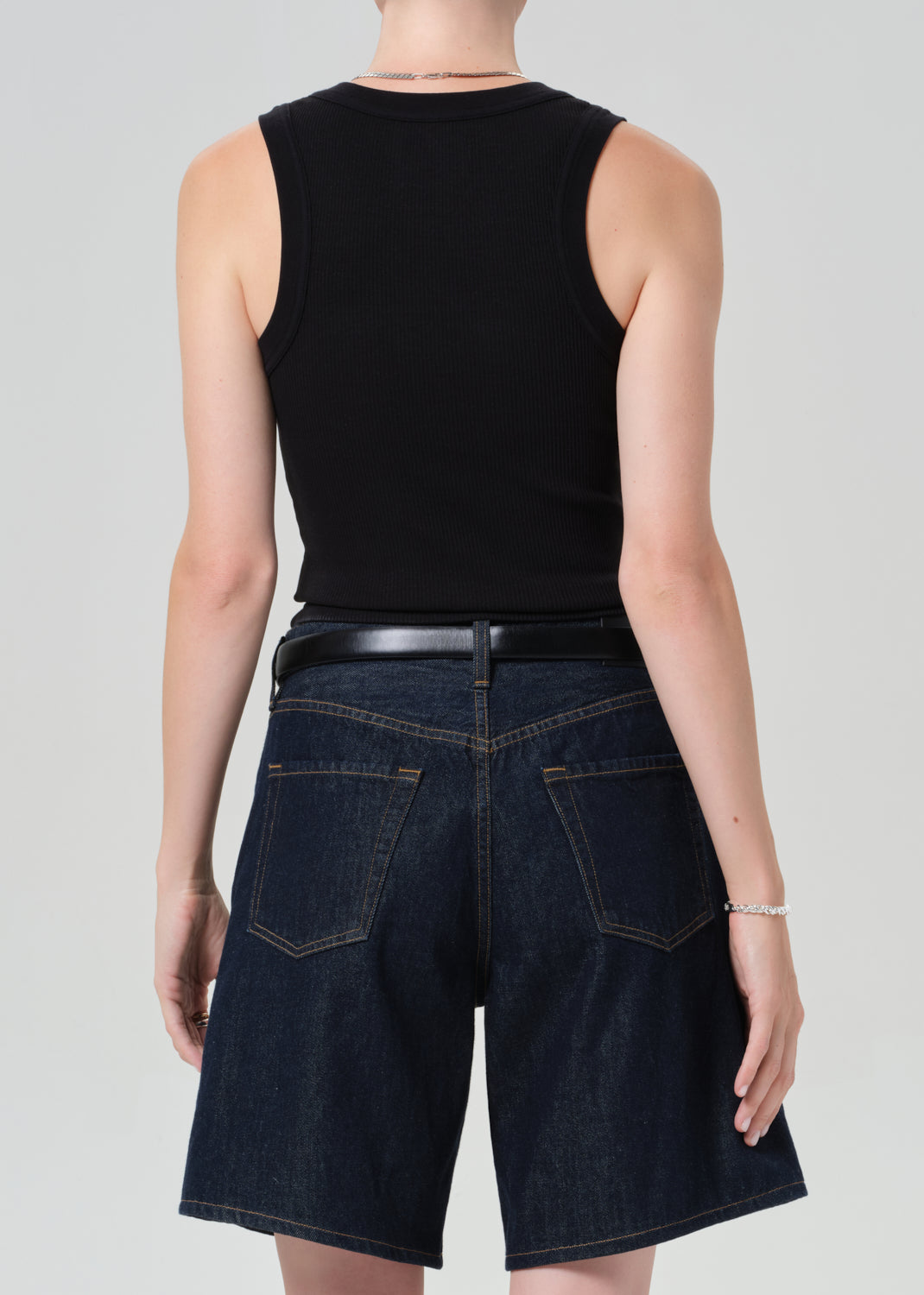 Person wearing a black sleeveless top and dark blue denim shorts on a gray background