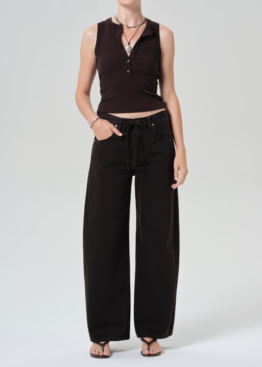 Person wearing a brown sleeveless top and brown pants on a light gray background