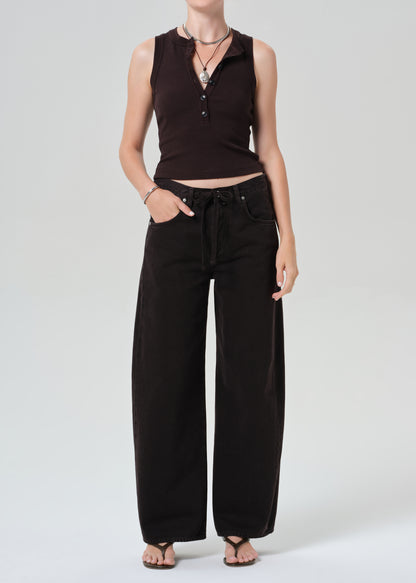 Person wearing a brown sleeveless top and brown pants on a light gray background