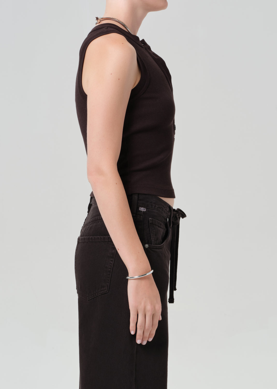 Person wearing a brown sleeveless top and brown pants on a light gray background