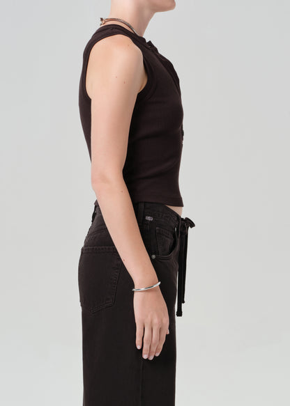 Person wearing a brown sleeveless top and brown pants on a light gray background