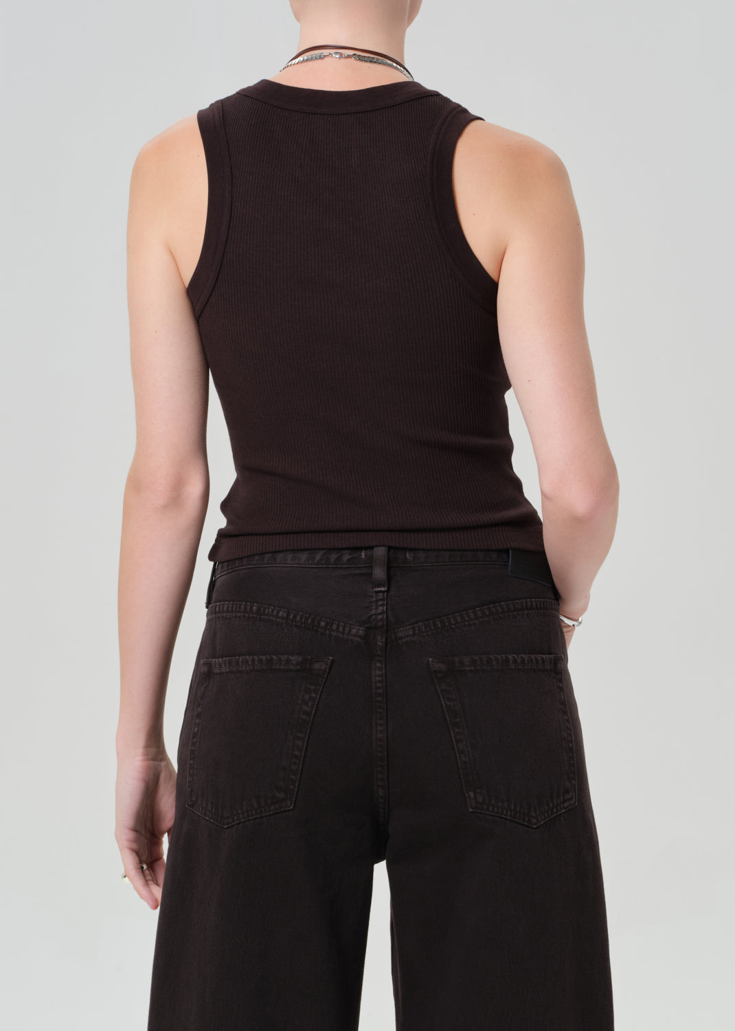 Person wearing a brown sleeveless top and brown pants on a light gray background