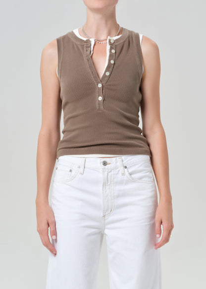 Person wearing a brown sleeveless top with buttons and white pants on a plain background