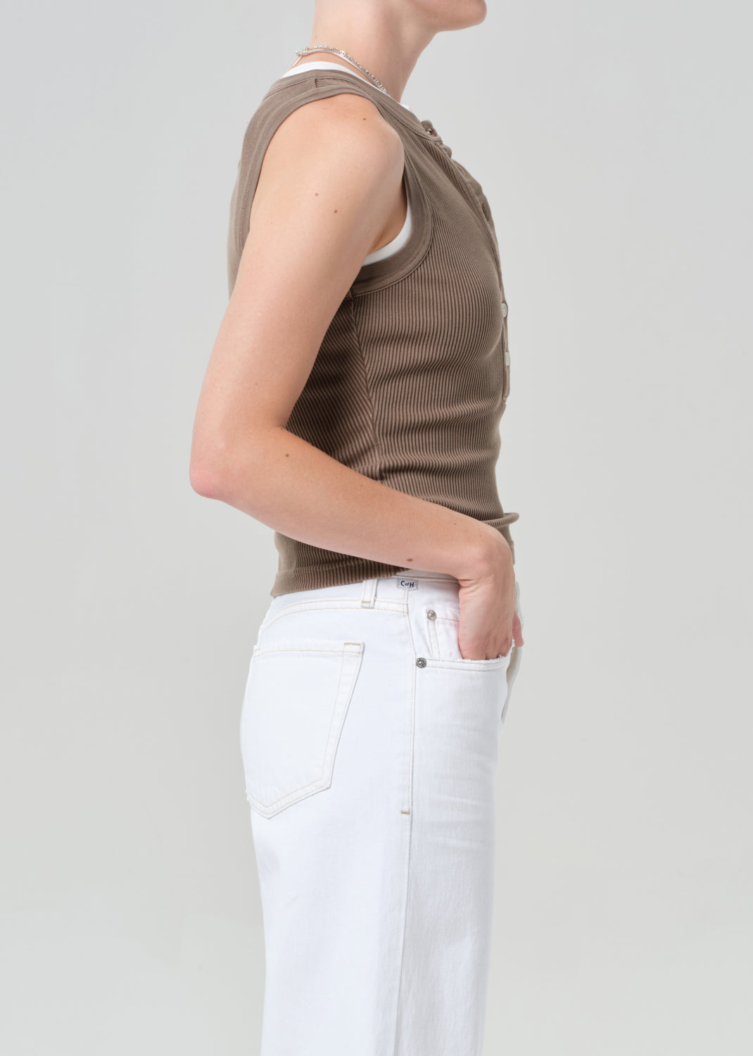 Person wearing a brown sleeveless top and white pants on a plain background