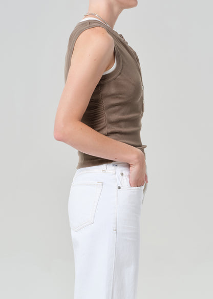 Person wearing a brown sleeveless top and white pants on a plain background