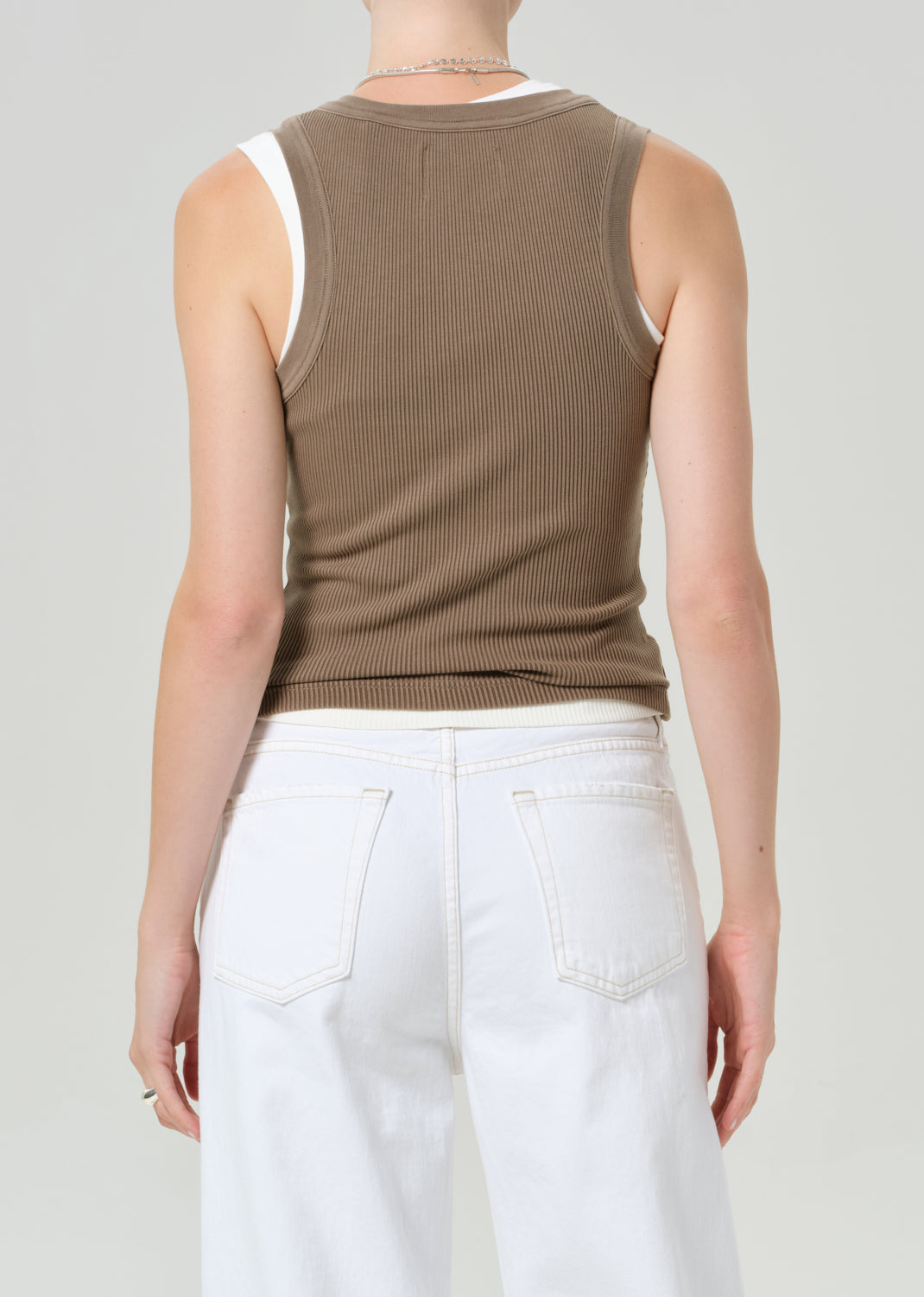 Person wearing a brown ribbed tank top and white pants on a plain background