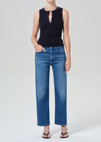 Person wearing a navy sleeveless top and blue jeans on a gray background