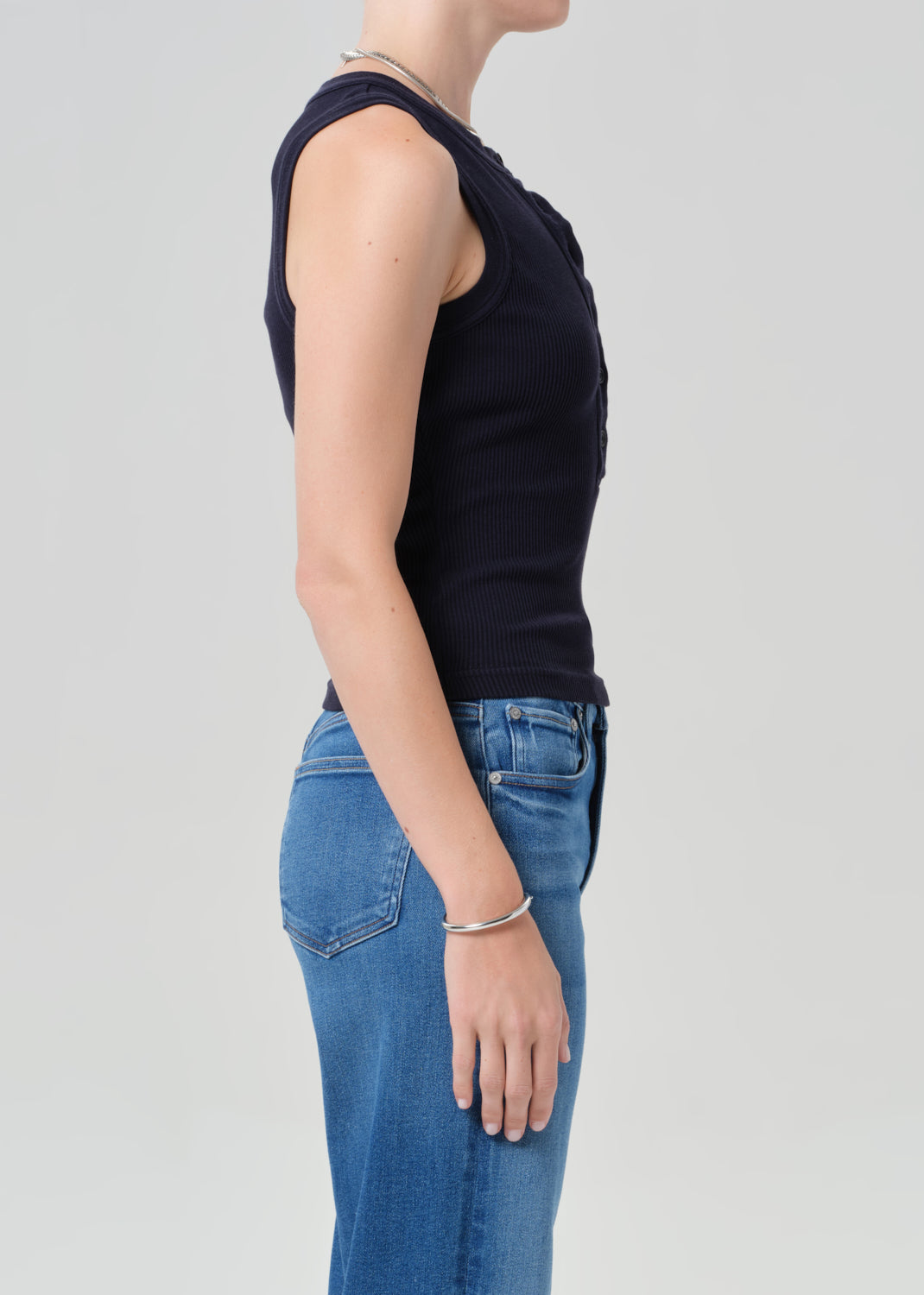 Person wearing a navy sleeveless top and blue jeans on a gray background