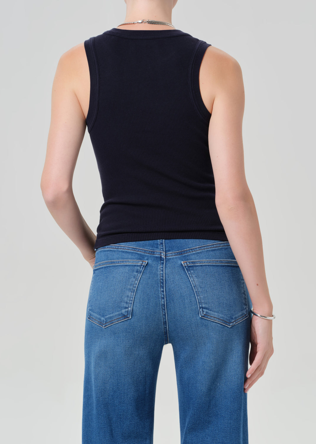 Person wearing a navy sleeveless top and blue jeans on a gray background
