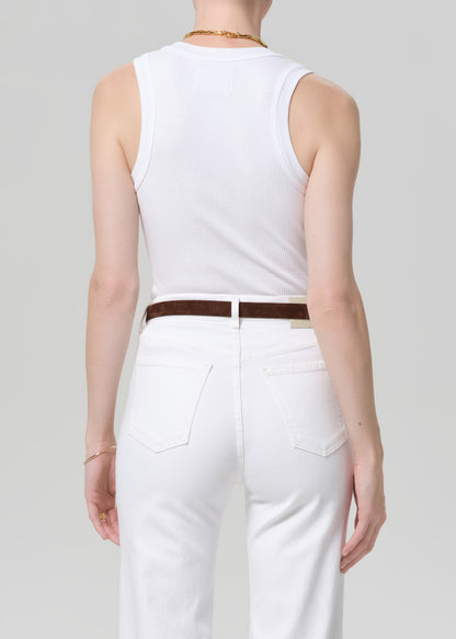 Person wearing a white sleeveless top and white jeans with a brown belt on a plain background