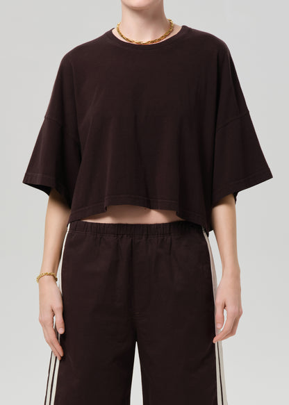 Person wearing a brown oversized t-shirt and brown shorts with white stripes on a light gray background