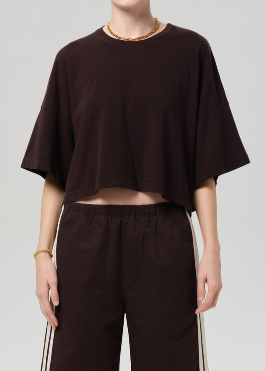 Person wearing a brown oversized t-shirt and brown shorts with white stripes on a light gray background