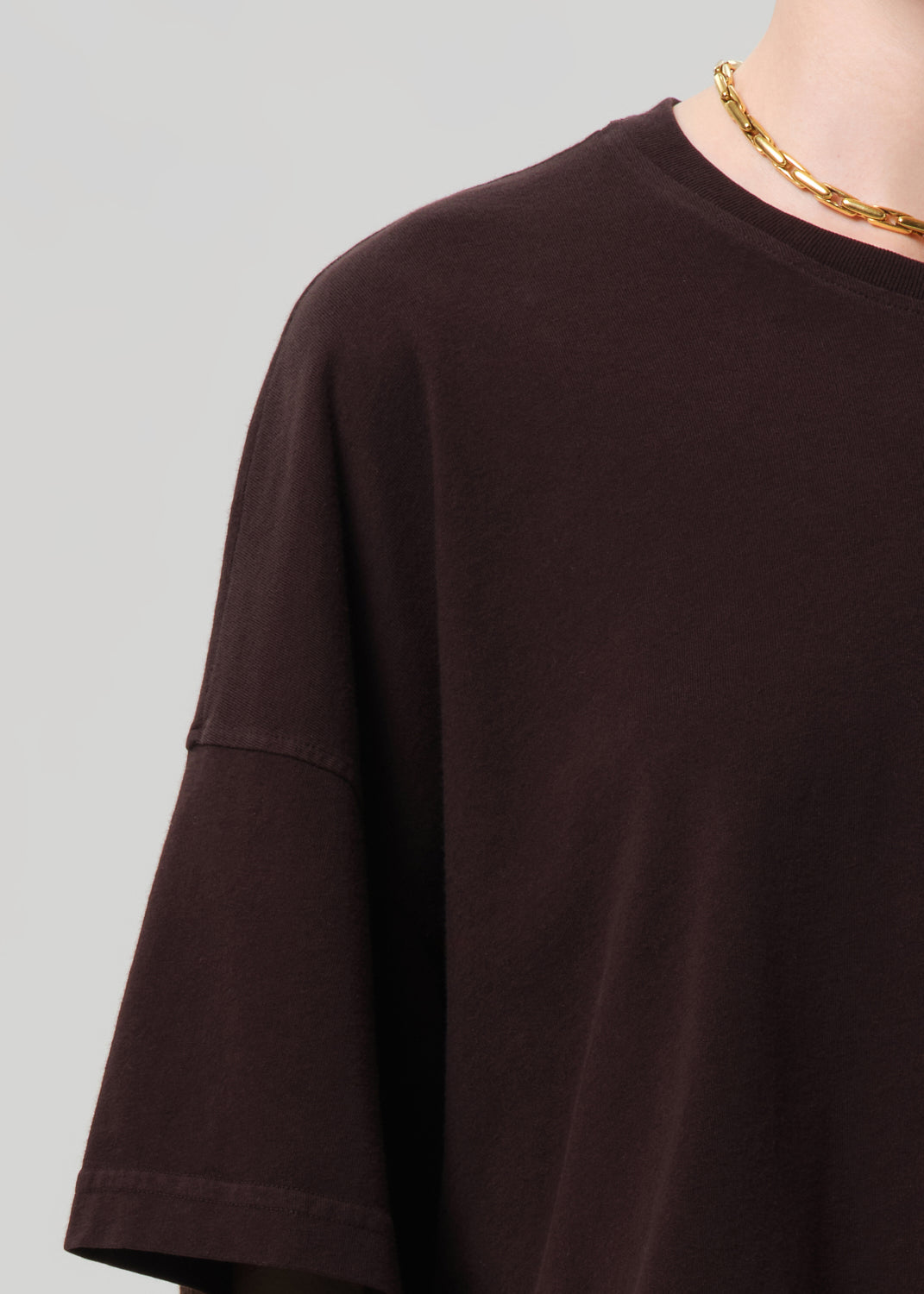 Person wearing a brown oversized t-shirt on a light gray background