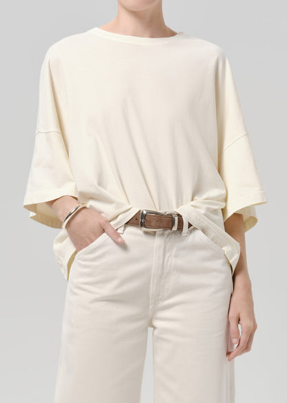 Person wearing a off white tee with white pants on a grey background
