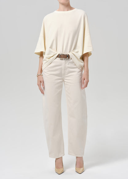 Person wearing a off white tee with white pants on a grey background