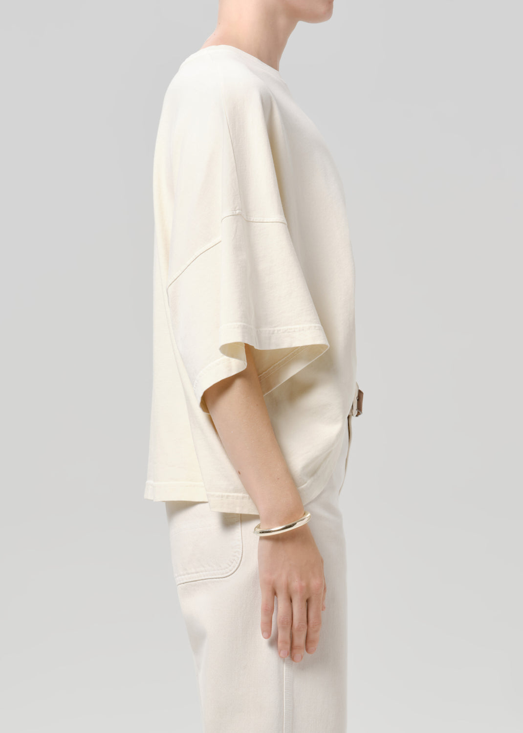 Person wearing a off white tee with white pants on a grey background