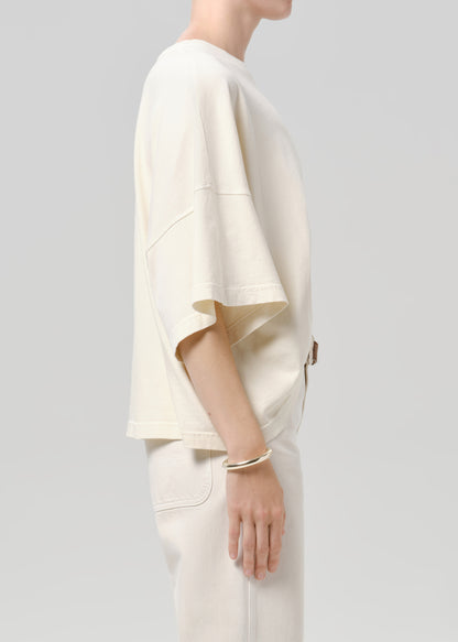 Person wearing a off white tee with white pants on a grey background