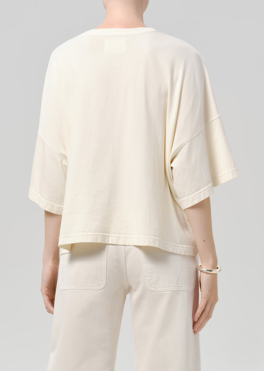 Person wearing a off white tee with white pants on a grey background