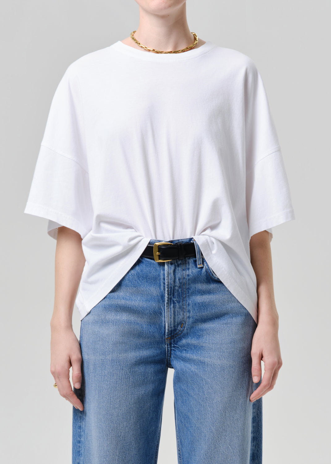 Person wearing a white oversized t-shirt and blue jeans on a grey background