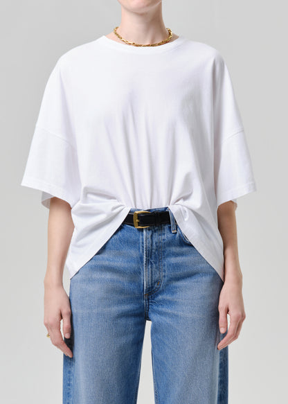 Person wearing a white oversized t-shirt and blue jeans on a grey background