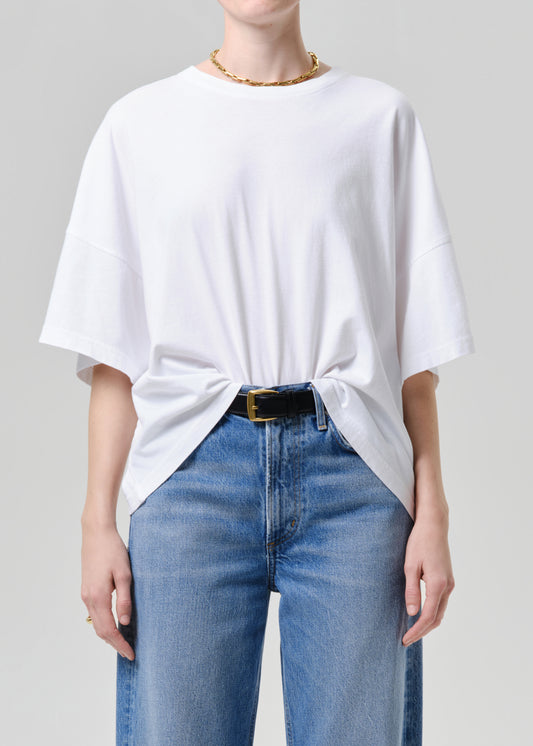 Person wearing a white oversized t-shirt and blue jeans on a grey background