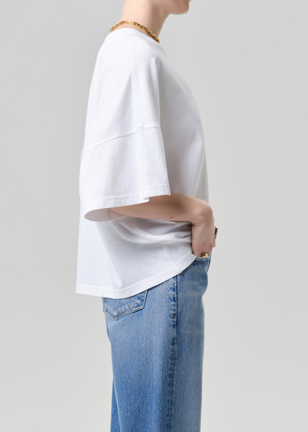 Person wearing a white oversized shirt and blue jeans on a grey background