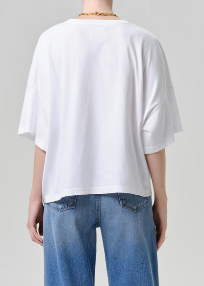 Person wearing a white oversized t-shirt and blue jeans on a grey background