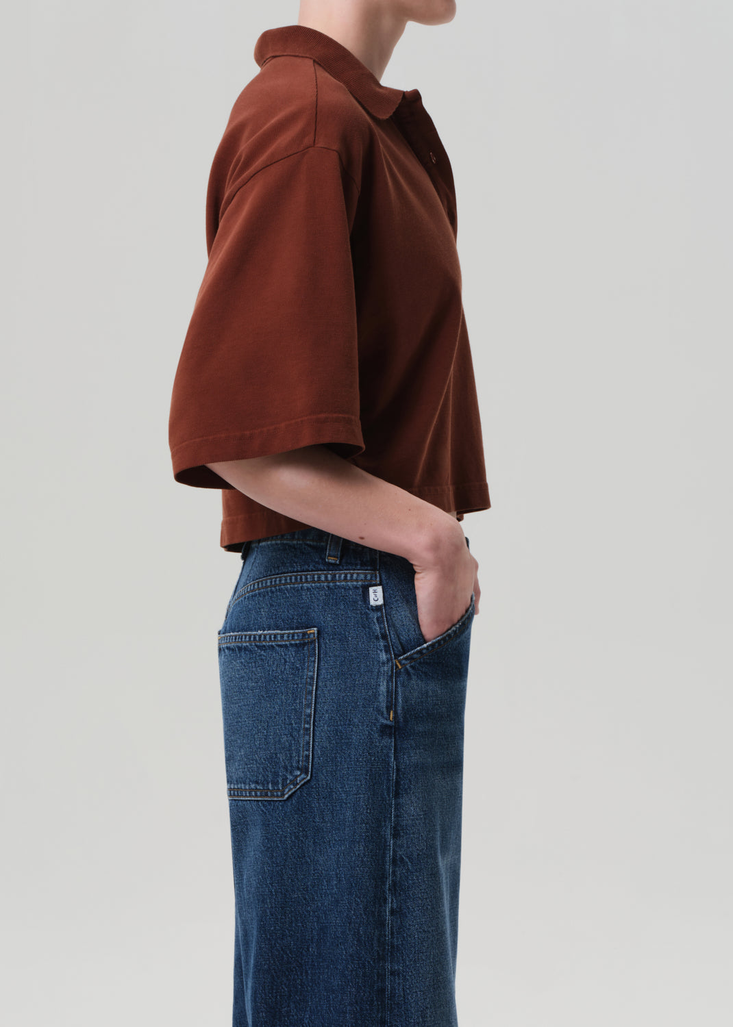 Person wearing a brown cropped polo shirt and blue jeans on a light gray background