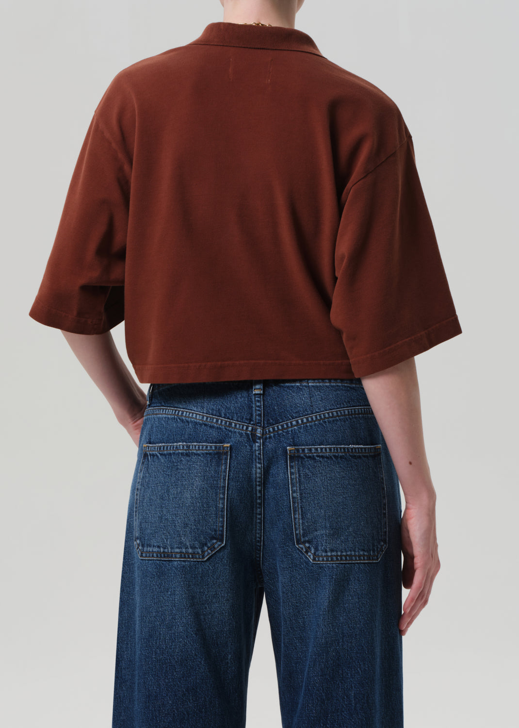 Person wearing a brown oversized shirt and blue jeans on a plain background